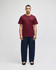 A model wearing a maroon short sleeve t-shirt and navy blue pants, standing against a plain background. The t-shirt has a logo.