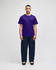 A model wearing a purple Champion adult jersey short sleeve t-shirt and dark blue pants, featuring a logo.