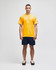 A yellow short sleeve t-shirt worn by a model, paired with navy shorts. The shirt features a small logo.