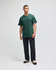 A green short sleeve t-shirt worn by a standing man, paired with dark pants and shoes. The shirt has a logo.