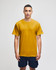 A man stands wearing a mustard yellow Champion Adult Jersey Short Sleeve T-Shirt with a logo, paired with navy shorts.