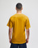 A back view of a mustard yellow short sleeve T-shirt on a model, featuring a logo on the upper back.