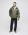 An olive green packable anorak jacket, featuring a hood and half-zip, worn by a model with black pants.