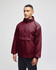 A maroon packable anorak jacket with a hood and a logo, worn by a model standing against a neutral background.