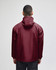 A maroon packable anorak jacket with a hood, viewed from the back, featuring a logo.