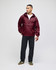 A maroon packable anorak jacket with a hood, worn by a model, paired with dark pants and green shoes.
