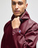 A maroon packable anorak jacket featuring a hood and adjustable cuffs, with a logo on the sleeve.