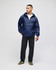 A model wearing a navy blue packable anorak jacket, paired with black trousers and green shoes. The jacket has a logo.