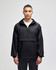 A black packable anorak jacket with a hood, featuring a front zip and a logo. Model is standing against a plain background.