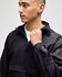 A black packable anorak jacket with a hood and logo, featured on a model facing slightly to the side.
