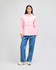 A pink packable anorak jacket with a hood, worn by a model paired with blue jeans. The jacket features a large pocket and has a logo.