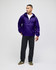 A packable anorak jacket in purple, featuring a hood and front pocket, worn by a model with dark pants and shoes.