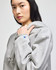 A grey cropped hoodie with a large hood and a logo on the sleeve, modelled by a woman.