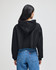 A black cropped hoodie with a hood, worn by a person facing away, paired with blue jeans.