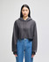 A grey cropped hoodie with a drawstring hood, featuring long sleeves and a logo on the cuff, worn with blue jeans.