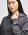 A model wearing a grey hoodie with a logo on the sleeve and a drawstring at the neck.