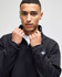 A man in a black quarter-zip pullover with a logo on the sleeve, posing against a neutral background.