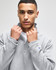 A grey quarter-zip pullover with a collar, featuring a branding logo on the sleeve.