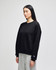 A black crewneck sweatshirt is displayed on a model, featuring a logo on the sleeve. The model wears grey pants.
