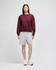A burgundy crewneck sweatshirt paired with grey shorts on a model, with white sneakers. The sweatshirt features a logo.