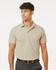 A men's polo shirt in light beige with a classic collar and short sleeves. The shirt features a logo on the chest.
