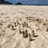 Wooden numbered skittle pins arranged in the sand on a beach, with hills and ocean in the background.