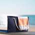 A navy waterproof beach bag with a woven handle and a folded orange and white towel draped over it.