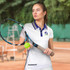 A woman wearing a white tennis top with a logo, holding a tennis racket and ball on a court background.