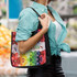 A black tote bag with a vibrant floral design, carried by a person wearing a green checkered shirt.