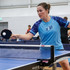 A woman plays table tennis, wearing a light blue custom active T-shirt with patterned sleeves.
