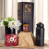 A festive essentials set featuring a black drink bottle, a candle jar, a gift box, and a flower arrangement.