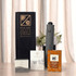 A grey umbrella stands beside packaged tea and coffee products, all displayed in a black box, with flowers in the background.