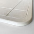 A light grey bath mat with a smooth texture and rounded edges, featuring subtle design lines. It has a branding logo.