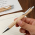 A pen with a wooden body and silver accents, held in a hand above a lined notebook.