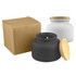 A black candle jar with a wooden lid next to a white candle jar, both with a brown box.