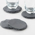 A set of four round slate coasters in grey with textured edges, featuring two glasses resting on them.