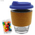 A glass coffee cup with a navy blue lid and cork band, accompanied by a pack of colourful jelly beans.