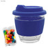 A reusable coffee cup with a navy blue silicone sleeve and lid, accompanied by a packet of colourful jelly beans.