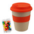 A bamboo cup in natural tones with an orange lid and sleeve, alongside a packet of colourful jelly beans.