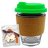 A glass coffee cup with a cork band and a green lid, accompanied by a pack of mixed lollies.