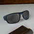 A pair of blue sunglasses with dark lenses rests on a light surface beside a brown case.