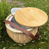 A round wicker picnic cooler basket in natural tones, featuring a wooden lid and a brown leather strap.