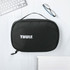 A black toiletry bag with a handle and a logo on the front, placed on a light wooden surface with office supplies.