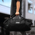 A black duffel bag with a mid blue accent and a logo, being held by a person.