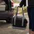 A foldable cooler in black and grey, held by a person near the back of a vehicle. It has carrying straps and a logo.