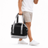 A foldable cooler in black and silver, carried by a person in shorts and a white shirt, with a logo visible.