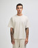 A unisex boxy t-shirt in a light beige colour, worn by a model with tattoos against a plain background.