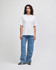 A woman stands wearing a white, heavyweight cotton, unisex boxy t-shirt paired with blue wide-leg jeans.