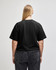 A black mid-length boxy top with short sleeves, displayed from the back on a model wearing light blue jeans.