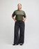 A woman stands wearing an olive green boxy top and light blue wide-leg jeans. The outfit is casual and stylish.